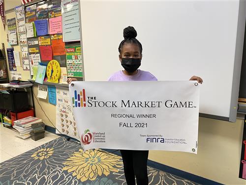 Student winner from Marley Elementary poses with winning banner for Stock Market Game